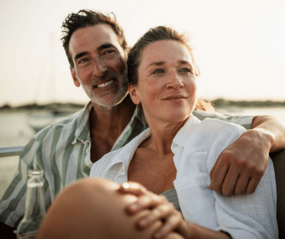 Couple sitting close on a boat, smiling and gazing toward the horizon with relaxed, affectionate body language
